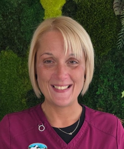 Jessica U, Customer Service Representative at MountainView Veterinary Hospital in Denville NJ, smiling in maroon scrubs in front of the green plant wall.